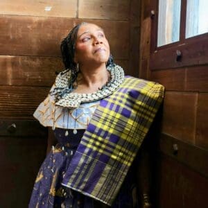 Woman in historical clothing gazes thoughtfully by a window.