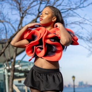 A young woman dances outdoors in a vibrant red top and black skirt.